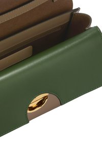 Zielona skórzana portmonetka o gładkim wykończeniu, z okrąłym złotym akcentem metalowym oraz jasnobrązowym wnętrzem z wieloma przegrodami.