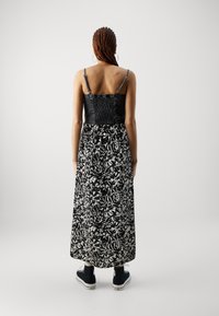 Maxime dress with a fitted black top featuring smocking. The skirt has a black and white abstract floral pattern. Paired with black sneakers.