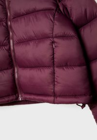Bordeaux pufferjakke med lynlås foran, der har et quiltet mønster, glat overflade og elastisk kant. Inkluderer justerbare stropper i bunden.