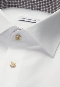 Chemise de ville blanche texturée avec boutons beige, col large, et doublure intérieure du col à motif laissant apparaître l'étiquette de la marque "seidensticker".
