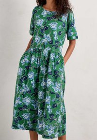 Robe verte avec un motif floral en bleu et des accents sombres, à manches courtes, encolure ronde et poches latérales. Texture semblable à du coton.
