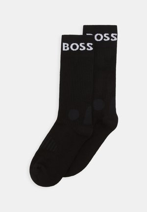 Schwarze Socken mit gerippter Textur, versehen mit einem weißen "BOSS"-Logo oben und dezenten schwarzen runden Akzenten nahe der Spitze.