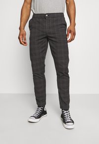 Pantaloni a quadri grigi in tessuto leggero, con vestibilità slim, chiusura con bottoni e tasche laterali, abbinati a sneaker nere in tela.