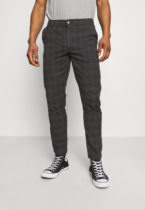 Pantaloni a quadri grigi in tessuto leggero, con vestibilità slim, chiusura con bottoni e tasche laterali, abbinati a sneaker nere in tela.