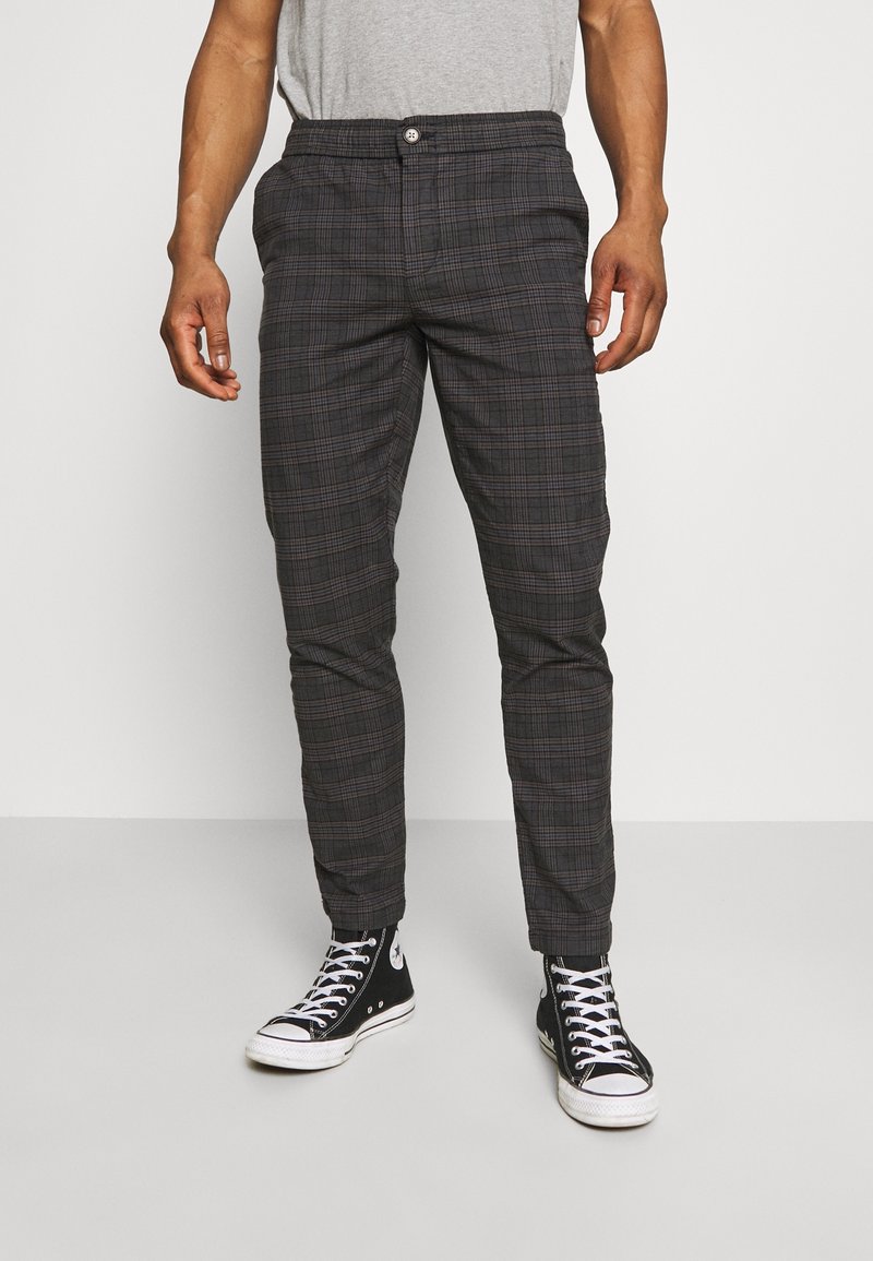 Pantaloni a quadri grigi in tessuto leggero, con vestibilità slim, chiusura con bottoni e tasche laterali, abbinati a sneaker nere in tela.