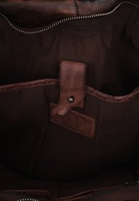 Dark brown fabric bag interior with leather trim and a small leather tab with a metal snap button inside a zippered opening.