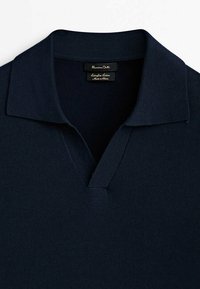 Polo en tricot bleu marine avec un petit col et une ouverture en V, montrant les étiquettes de la marque et du tissu à l'intérieur de l'encolure.