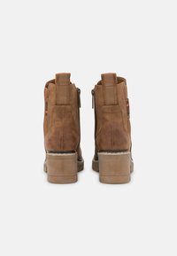 Braune Wildleder-Stiefeletten mit einem Blockabsatz, ausgestattet mit doppelten seitlichen Reißverschlüssen und elastischen Einsätzen für einfachen Zutritt. Texturierte Oberfläche.