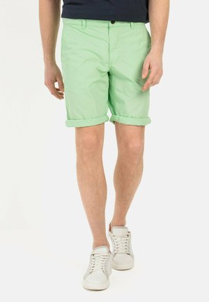 Mintgroene shorts met opgerolde zoom en knoopsluiting, gecombineerd met witte veterschoenen. Het materiaal lijkt lichtgewicht en soepel.