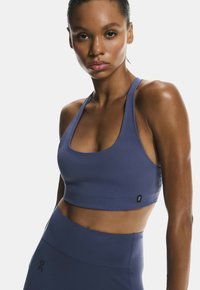 Sujeta de deporte hecha de una tela suave y elástica en azul profundo, con tirantes anchos, escote en forma de barco y un pequeño logo en el dobladillo.