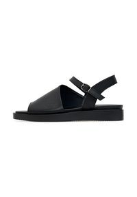 Sandelă neagră cu superior din piele, vârful deschis și curea de tip slingback. Prezintă o talpă plată și o cataramă ajustabilă pentru o fixare sigură.