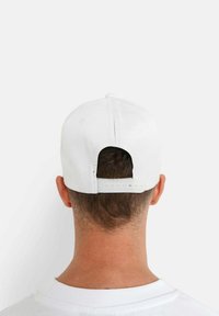 Weißer Baseballhut mit einem gebogenen Schirm und verstellbarem Snapback-Verschluss. Glattes Material und minimalistisches Design, mit sichtbaren Stickdetails.