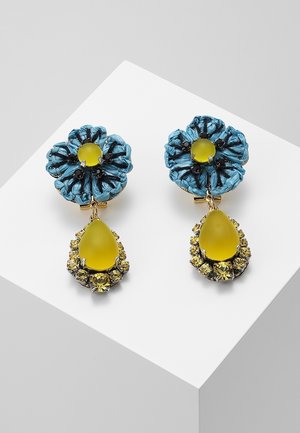 Niebieskie kolczyki w kształcie kwiatów z czarnymi detalami i żółtymi kamieniami w kształcie kropli otoczonymi mniejszymi żółtymi kryształkami, osadzone na białej powierzchni.