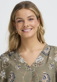 Olivrohelises lillemustriga kleit, millel on V-kaelus ja patsisarnased varrukad. Kangal on õrn tekstuur ja keerukad lillemustrid.