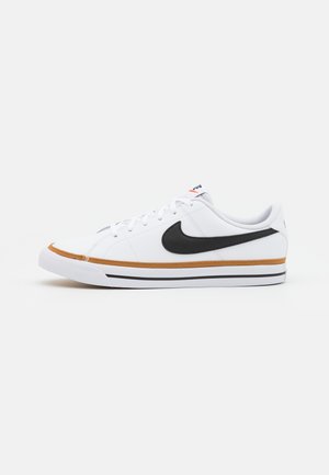 Bílé tenisky Nike s černým logem, hnědými akcenty na podrážce a bílými šňůrkami. Mají hladký povrch a nízkoprofilový design.