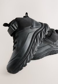 Čierne vysoké športové topánky s textúrovanými panelmi, gumovou podrážkou s vzorom a systémom zapínania na šnúrky a suchý zips.