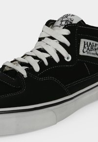 Μαύρα παπούτσια skateboard Vans Half Cab με λευκά κορδόνια, λευκά ράμματα και λευκή σόλα.