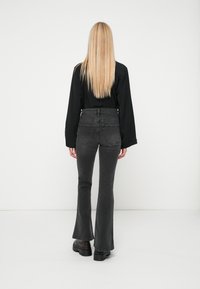 Juodas ilgomis rankovėmis viršus, derinamas su aukštu juosmeniu, platėjantis tamsiai pilkas džinsas. Glotni tekstūra su šiek tiek tamprumo, turintis dvi užpakalines kišenes.