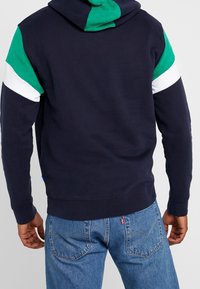 Felpa navy con maniche a blocchi di colore verde, bianco e nero, caratterizzata da una vestibilità classica e un morbido materiale in cotone. Etichetta blu sul lato.