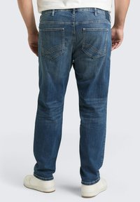 Dunkelblaue Jeans mit lockerer Passform. Sie verfügen über zwei Gesäßtaschen mit geschwungenen Stichdetails und einen klassischen Bund. Weiße Sneaker werden getragen.