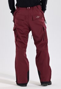 Burgundy cargobyxor med rak passform, flera fickor och svarta detaljer vid bensluten. Tillverkade av ett hållbart, elastiskt material.