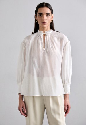 Blouse blanche à manches longues avec une coupe décontractée. Présente un col froncé avec une fermeture à nouer et des poignets élastiqués. Tissu doux et léger.