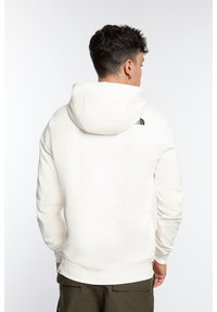 Sudadera blanca de algodón con una capucha amplia, puños y dobladillo acanalados. Presenta un pequeño logo negro en la parte superior de la espalda. Textura suave.