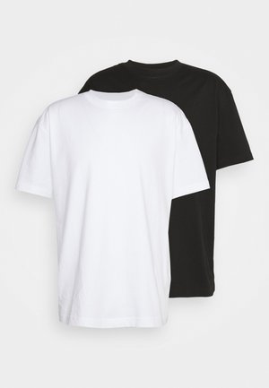 Bawełniane koszulki w kolorze białym i czarnym, z krótkim rękawem, okrągłym dekoltem i luźnym krojem. Biała koszulka znajduje się z przodu czarnej.