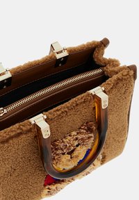 Borsa marrone con texture e superficie pelosa, caratterizzata da un motivo orso. Finiture in tonalità oro, chiusura con zip superiore e manici in tartaruga.