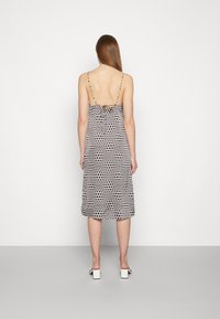 Vestido sem mangas com um padrão de bolinhas em preto e creme. Apresenta um design nas costas com laço e chega até à panturrilha. Textura de tecido suave.