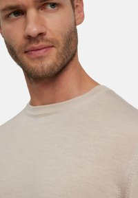 Helles beiges Sweatshirt mit glatter Textur, rundem Ausschnitt und gerippten Details am Kragen, das eine Nahaufnahme des Stoffes zeigt.