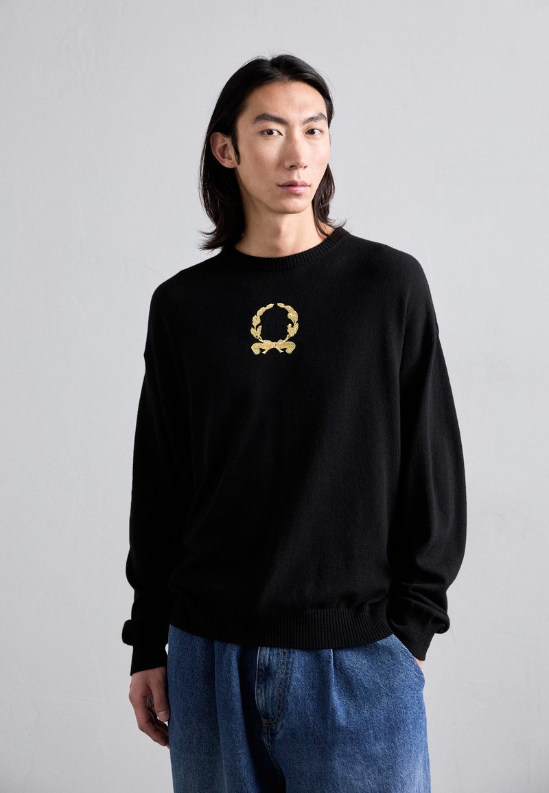 Schwarzer Pullover aus weichem Stoff, mit einem goldenen gestickten Lorbeerdesign auf der Brust. Lockere Passform mit gerippten Bündchen und Saum.