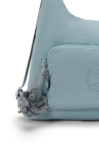 Light blue shoulder bag with a front pocket, zipper, round brand logo, and a small gray plush gorilla keychain attached.