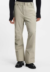 Wodoodporne spodnie narciarskie w kolorze khaki o prostym kroju nogawek, wzmocnionych mankietach i czarnych detalach metalowych. Materiał ma gładką teksturę.