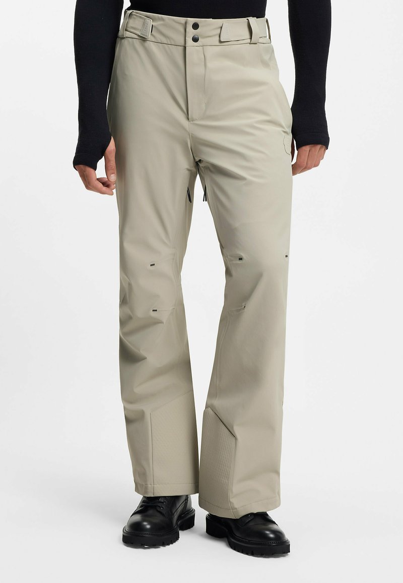 Wodoodporne spodnie narciarskie w kolorze khaki o prostym kroju nogawek, wzmocnionych mankietach i czarnych detalach metalowych. Materiał ma gładką teksturę.