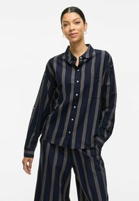 Camisa de botones color marino con rayas verticales blancas, de manga larga y con cuello. Tejido suave con un corte holgado y un solo bolsillo en el pecho.