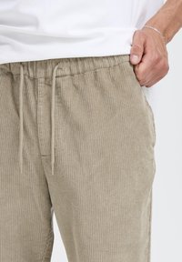 Beige corduroy pants with a ribbed texture, an elastic waistband, and drawstring closure; front pocket visible at the side.