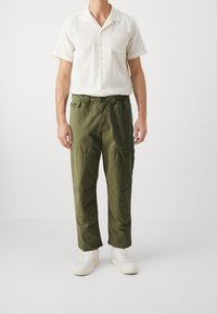 Short-sleeve white shirt with textured stripes and pocket, paired with olive green cargo pants featuring multiple pockets, worn with white sneakers.