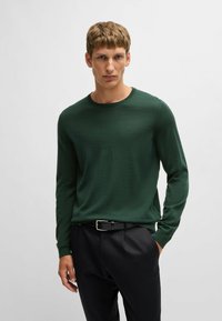 Maglione verde a maniche lunghe in maglia con scollo rotondo, abbinato a pantaloni neri e a una cintura nera con fibbia argentata.
