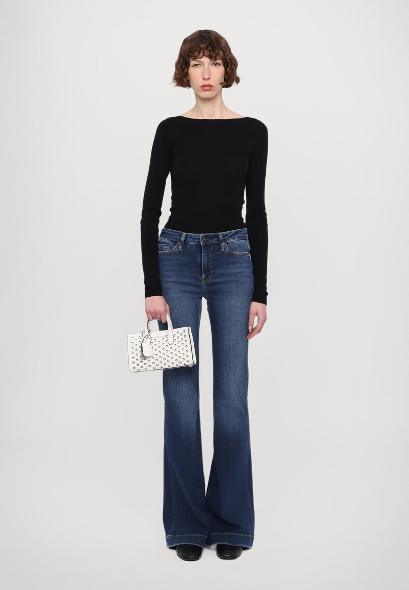 Top nero a maniche lunghe, jeans svasati blu a vita alta, borsa bianca con borchie circolari e scarpe nere eleganti.