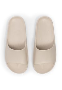 Beige slide-sandaler med en glat overdel af kunstlæder og tekstureret sål. Åben tå-design, flad sål, minimalistisk form.
