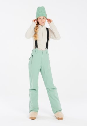 Pantalons de ski vert menthe avec bretelles noires ajustables, un haut en polaire beige clair, et un bonnet en tricot texturé vert menthe.