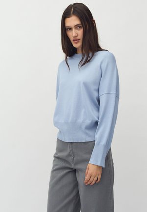 Light blue knitted sweater with a relaxed fit, rounded neckline, and long sleeves. Paired with grey wide-legged trousers. Smooth texture.