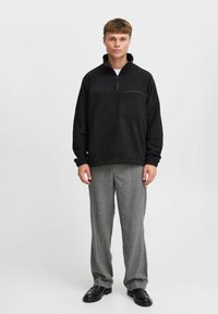 Pullover in fleece nero con colletto zip e tasca frontale. Indossato con pantaloni a quadri grigi e scarpe nere. Design semplice e dalla vestibilità rilassata.