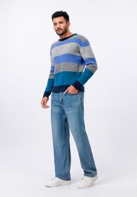 Jersey de punto a rayas azul y gris con textura de canalé, combinado con pantalones vaqueros azul claro y zapatillas blancas. Diseño de cuello redondo sencillo.