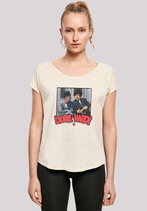 Cream-colored short-sleeve t-shirt featuring a graphic of two men in bowler hats with "LAUREL & HARDY" text in red. Soft texture.