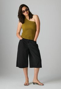 Top en verde oliva, de un solo hombro y con tejido texturizado; combinado con culottes negros de pierna ancha; la modelo lleva gafas de sol y tacones de tiras.