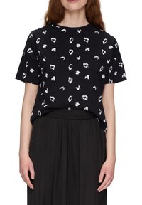 Zwarte t-shirt met een losse pasvorm, met een witte abstracte patroon. Korte mouwen en ronde halslijn. Draagt met een zwarte, vloeiende rok.