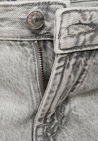 Grå denimtyg med ett vertikalt mönster, med en metallknapp och dragkedja. Nära bild av midjebandet och dragkedjeområdet.