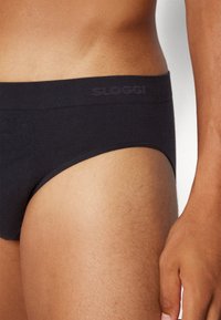 Schwarze, enganliegende Boxershorts mit glatter Textur, versehen mit einem dezenten Logo am Bund. Auf der Haut präsentiert, um die Passform deutlich sichtbar zu machen.